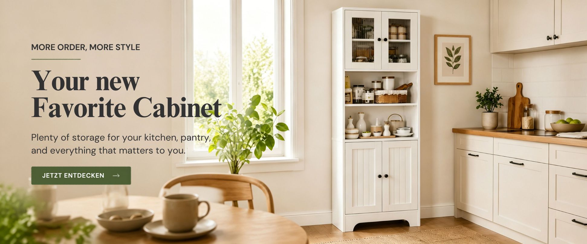 Modern white kitchen cabinet with two glass doors on top, open shelves in the middle, and closed doors below, filled with dishes, pantry items, and decorative elements. In the bright kitchen, a table with a cup and plant on the left, countertop with potted plant and framed artwork on the right.